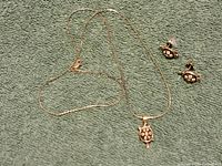 Full view of the sterling silver turtle pendant necklace and matching turtle stud earrings laid on green fabric with a coin for size reference.