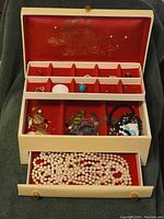 Full jewelry box showing three levels: top compartment with rings and small items, middle with earrings and brooches, and bottom drawer with pearl necklaces.