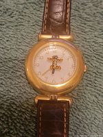 Close-up of watch face showing Tigger character with arms as watch hands, gold-tone casing and numbers, mounted on a brown leather strap.