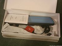 Smart rearview mirror with blue reflective surface and attached cables inside an open white box.
