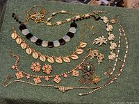Full view of the jewelry lot on a green cloth displaying multiple necklaces, brooches, earrings, and a bracelet.