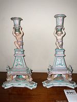 Full pair of porcelain candlesticks displayed side by side on wood surface with sticker visible
