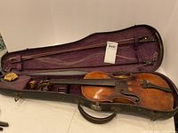 Open case showing violin body in lower compartment and two bows in upper lid