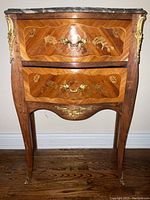 Front view of marble top commode with two drawers, floral marquetry and ormolu mounts