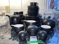 Overall view of matte black Hornsea Image dinnerware set including stacks of plates, bowls, cup, teapot, sugar bowl, creamer, salt and pepper shakers