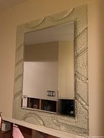 Full view of the rectangular molded glass framed mirror hung on a wall, showing textured frame with curved raised details on the top and sides.