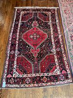 Full view of red and dark blue Persian rug with central medallion on hardwood floor
