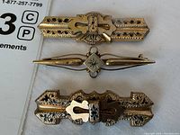 Three brooches stacked vertically showing front designs