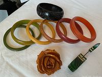Seven Bakelite bangles arranged in front of a large carved Bakelite bangle, plus a carved rose brooch and green stick pin
