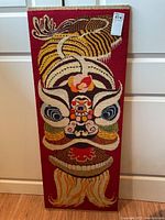 Full view of the rectangular needlepoint wall hanging showing entire stylized lion head design on red background.