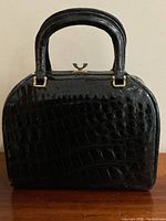 Front view of black crocodile-embossed leather handbag with structured silhouette and double top handles