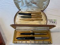 Two Parker presentation cases open showing four gold-filled pens in upper case and two pens in lower case