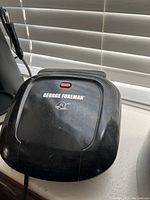 Top view of the black George Foreman Panini maker showing the red indicator light and logo on lid.