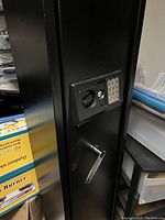 Close-up image of the front of a black gun safe showing digital keypad, key lock, and manual crank handle
