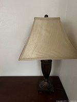 Front side of a brown and beige table lamp showing fabric shade and decorative dark brown base with vertical carved lines.