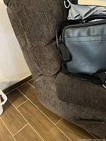 Brown fabric recliner chair with textured upholstery, partially shown from the side with some items on top.