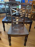 Six dark brown wooden dining chairs arranged in display, showing front and side views with cross backs and turned legs.