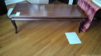 Full view of the wooden coffee table showing its rectangular top and curved legs on a hardwood floor.