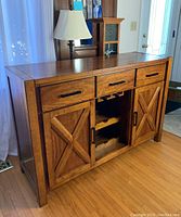 Front angle view of the oak veneer dining room server showing 3 pull drawers on top, center bottle storage with racks, and 2 X-paneled doors on the sides