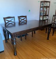 Full view of the rectangular wooden dining table with spindle legs and chairs around it, showing the dark wood finish and detailed legs.