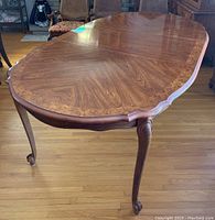Oval wooden dining table with decorative scalloped edges and claw style legs from a side angle showing detailed wood grain and leg design.