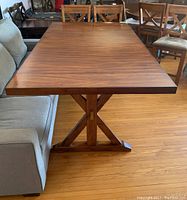 Rectangular dining table with oak look veneer finish and central cross-style pedestal base, close-up side angle, some scratches visible.