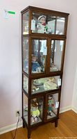 Full view of the tall wooden display cabinet showing four separate glass-fronted display sections with dolls inside (contents not included in sale).