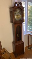 Full height view of the traditional wooden grandfather clock against a wall, showing overall design and condition.