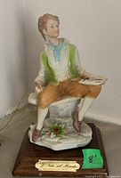 Front view of the porcelain figurine depicting a seated man in period clothing, holding a sketchbook, mounted on wood stand with 'L'Arte nel Mondo' plaque.