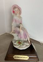 Front view of the porcelain lady figurine seated on rock base with wooden stand and brass plaque