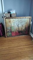 Front view of the large framed abstract print showing tree imagery and textured colorful background in a gold frame.