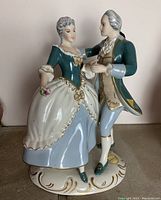 Front view of the porcelain dancing couple figurine, showing detailed facial features, clothing, and base decoration.