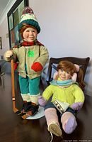 Front view of the two porcelain sports-themed dolls, one standing hockey player and one seated figure skater