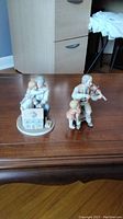 Porcelain figurines on wooden table showing detailed figures of grandparent with children, one with violin