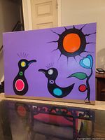 Full view of front of painting featuring two black stylized birds, an orange sun, blue heart motif, and red berry on a purple background
