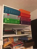 Seven shelves filled with various crafting supplies and multi-colored plastic storage bins on top shelf. Spiral notebooks and books in the middle shelves. Miscellaneous crafting items and boxes below.