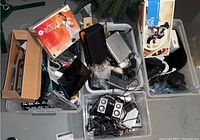Four bins containing assorted electronic devices and accessories including Wii related items, cords, and other equipment