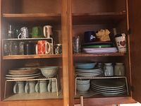 Full view of cabinet with stacked Fitz and Floyd plates, bowls, mugs, plastic plates and glasses.