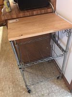 Front and side view showing wooden top and metal wire shelves of kitchen cart on caster wheels.