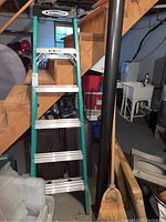 Full view of the green Werner step ladder showing six aluminum steps, leaning against wooden stairs in a basement space.