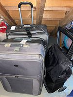 Three wheeled suitcases shown together: the gray Maestro luggage in front, another large suitcase behind, and the black mesh rolling trolley on the right
