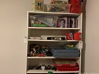 Five shelves of items including plastic bins with toys and craft supplies, Elvis lunchboxes, microscope kit, slide making kit, and loose items.