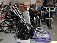 Full view of three black wheelchairs, crutches, Aircast boot, and other mobility supplies in basement setting