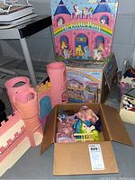 Open cardboard box showing pink castle pieces and loose ponies