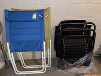 Four folded chairs grouped; two with white frames and canvas, two black metal folding chairs.