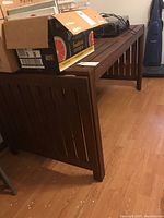 Angled view of dark wooden slatted patio table with cardboard boxes on top in indoor setting