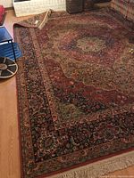 Full view of rug laid on hardwood floor showing central pattern, colors and fringe