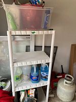Full view of the white plastic four-tier shelf in garage with cleaning and gardening items arranged on shelves.