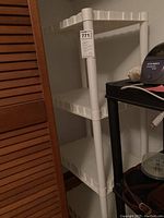 White Fortier 4-tier plastic shelf with wavy shelf edges and rounded legs in corner of a closet.