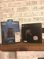 Front view of boxed Sirius XM XMp3i Portable Satellite Radio with Home Kit and Ecobee 3 Wi-Fi Thermostat box on shelf against brick wall